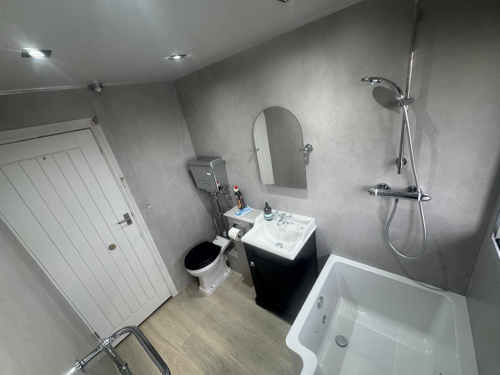Bathroom refit with grey wall panels, shower bath, traditional high-level toilet and navy vanity unit