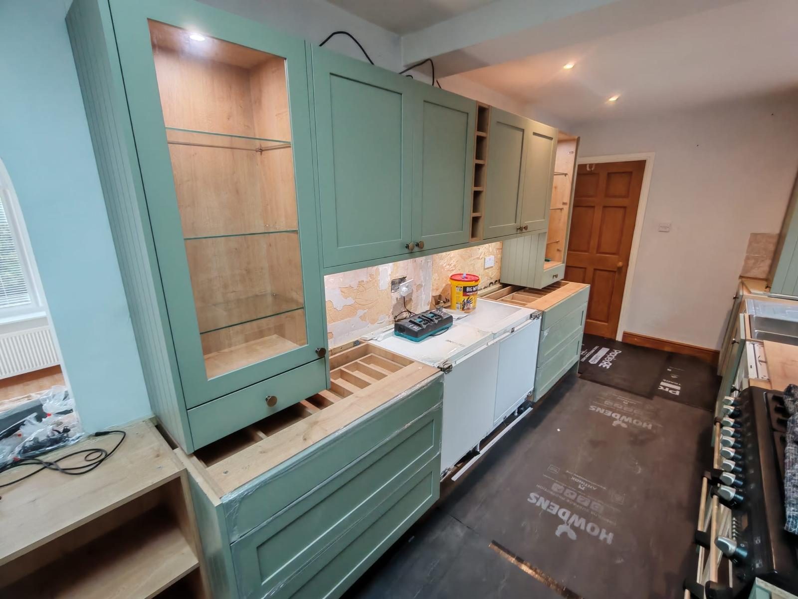 Sage green shaker kitchen with lit glass display cabinet being fitted