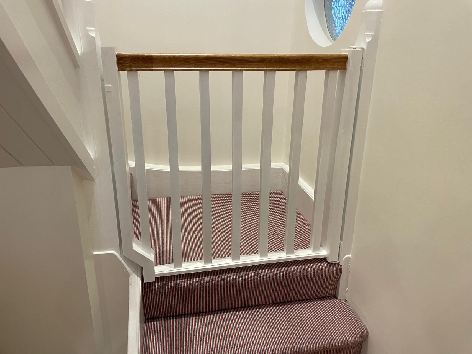 Bespoke white stair gate with oak handrail made to fit an angled staircase