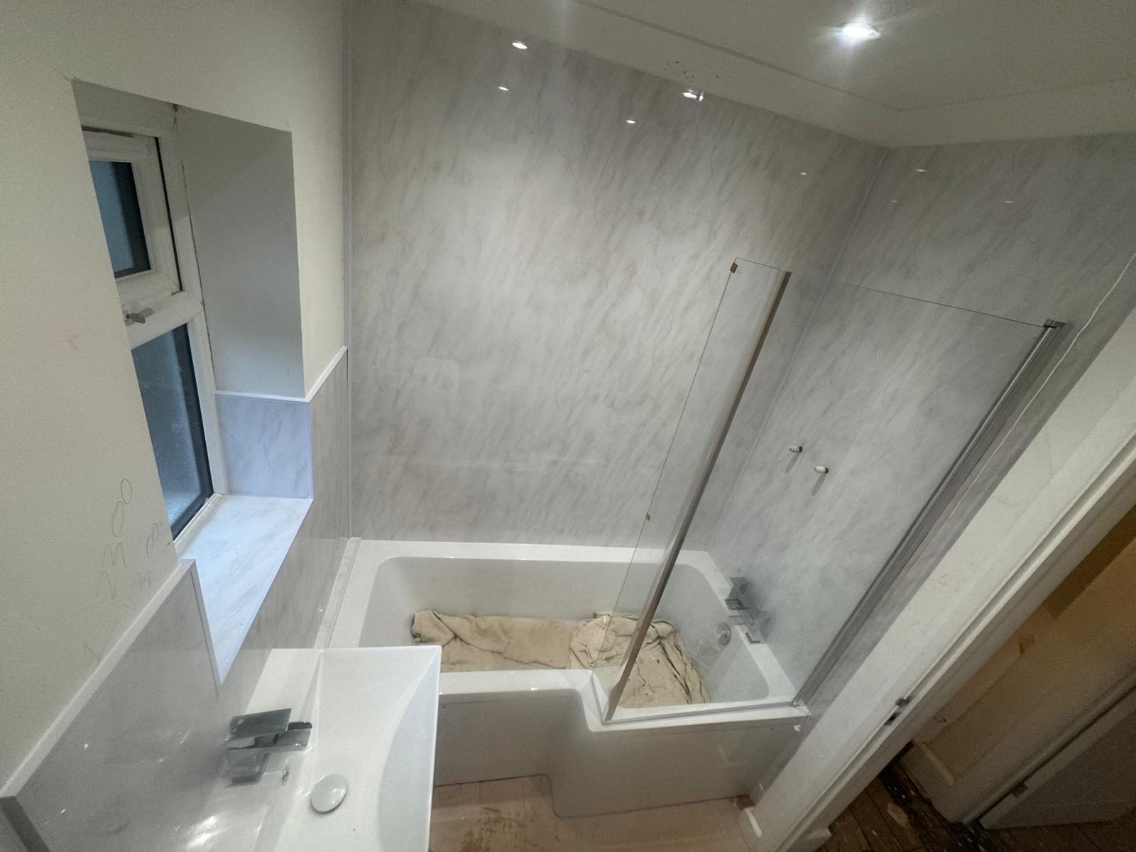 Bathroom refit with marble-effect wall panels, shower bath and glass screen