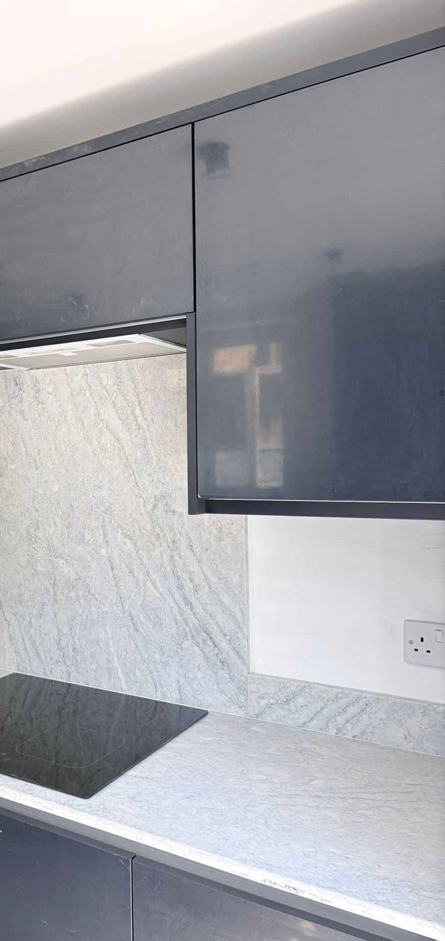 Granite splashback and induction hob beneath gloss wall units, fitted kitchen